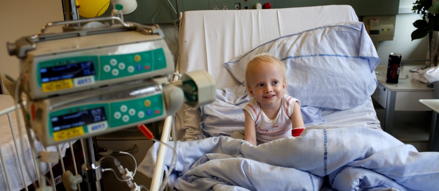 Smilende lille pige sidder med sin far i en hospitalsseng